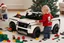 Placeholder: A crying toddler takes a burning car out of a LEGO box marked Land Rover next to the Christmas tree.