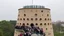 Placeholder: Conical tower with lots of randomly placed round windows, viewing platform on top, long queue of people waiting to go in, award-winning photograph, exquisite realism