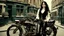 Placeholder: full-height portrait of a woman with straight shoulder-length black hair, with metal arms and legs, dressed in leather trousers, and a waistcoat, in a Victorian street next to a steampunk bike