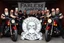 Placeholder: a very hard and tuff motorcycle bald gang, not old, posing with their Harley Davidsson bikes, some of them holding guns and shotguns, a logo sign with Falköpings HD Club, "Fearless sinners" Skulls and bones, skeletons
