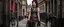 Placeholder: full-height portrait of a woman with straight shoulder-length black hair, with metal arms and legs, dressed in leather trousers, and a waistcoat, in a Victorian street next to a steampunk bike