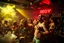 Placeholder: dans golv på en nedsliten sunkig techno club, många personer som dansar, yppiga kvinnor, mycket scen rök i lokalen, och gula röda strobes, en del personer ser in i kameran och skriker: "Benny!" och en Neon Skylt med texten "DJ ROY" på väggen, DJ Roy skriker rätt in i kameran, öppen mun, mycket flaskor och glas i baren