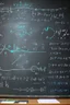 Placeholder: Subatomic particles writing equations on a chalkboard, while educating human children sitting at desks