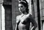 Placeholder: [photo by helmut newton in agent provocateur on the arena] Her complexion, after years spent training under the sun, bore the mark of a warrior who had weathered countless battles. Though her face spoke of hardship, there was also an air of grace and serenity that emanated from her every pore. Selene's physique was a testament to her dedication and discipline. Her muscular frame hinted at her physical prowess, yet her movements were fluid, as if she danced with the wind itself.