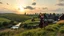 Placeholder: a lady dancing to camera in village over high grassy hills,a small fall and river and wild flowers at river sides, trees houses ,next to Ripe wheat ready for harvest farm,windmill ,a pretty train is arriving to station along river,a few village local shops ,cloudy sun set sky