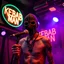 Placeholder: a very thin swedish man, with a skimask with only a hole for the mouth (no eyes), he is called "KEBAB MAN" performing at death metal club, his name is "KEBAB MAN" kebab rolls On stage, kebab Neon lights and smog, and "KEBAB MAN" big sign on the wall, kebab tribal tattooes, spinning kebab machines, flames and smoke, chaos, he singing with mic,