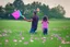 Placeholder: a father, a girl and a boy with a kite flying in the sky on the green field with flowers in sunshine