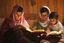 Placeholder: A close-up scene of an Arab mother reading the story from a book with her children around her in the room of the old wooden house near the fireplace 100 years ago.