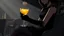 Placeholder: midle close up gray-toned, contrasting graphics, a lady in a black casual dress, black lace nice nylon stockings sitting on a bar chair in bar, holding a yellow mimosa cocktail in her long black gloved hand, atmospheric, strong contrasts, shadowy background, focus on the hand holding the cocktail, moody, pale ligts, anime style, cinematic