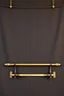 Placeholder: darker textured hanging fabric background with decorative brass corners at top, and a wide decorative brass bar clamped across the bottom