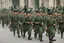 Placeholder: caucasian soldiers; marching in formation; facing away from camera; military parade; tight formation; shoulder to shoulder; marching along a street; green uniforms; medals and insignia; weapons in hands;