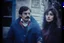 Placeholder: a young man and a beautiful woman standing next to each other, 1 9 8 0 s analog video, with mustache, assyrian, small glasses, cold scene, out of focus background, house on background, the woman has long dark hair, the photo shows a large, deiv calviz, before the final culling