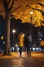 Placeholder: night yellow lights over the street trees autumn leaves under feet ,a Student adult girl with books in her hand walking in street looking to camera a boy walks after she few meters away her back