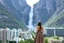 Placeholder: A modern city at the foot of the mountain. The entrance valley with a waterfall from a high rock. A beautiful lady in a top and midi skirt.