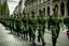 Placeholder: Soldiers marching in formation; military parade; marching along a street; green uniforms; medals and insignia; Rifles in their hands;