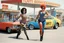 Placeholder: one woman in bright colorful and checkered (high res photo by Ralph Steadman in the 70ties) super heroine in leotard (chevron, lycra, nylon, spandex, tights) stops a massive violent thief at a gas stations, she is the queen of jujustu