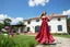 Placeholder: full body close up shot ,country side modern villa wide yard in front of villa ,a beautiful lady in nice long dress dancing,flowers blue sky ,petty clouds