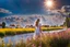 Placeholder: Young woman in flower field in country side ,river, houses,blue sky ,nice clouds,god rays