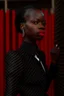 Placeholder: Tall darkskinned woman in black suit; side view, red lips, 16K, image photographic, and behind teh woman a tangle of mesh in the background