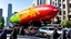 Placeholder: cartoonish jesus parade blimp hybrid , pulled by multiple grim reapers, multi colored, bright, vivid, psychedelic, high detailed, high gloss, insanely detailed, matte, horrorcore, lining the street, unsettling contrast, monument to death, live action shot grim reaper parade, pulling a jesus parade float