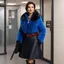 Placeholder: [in a police office] a brunette 40 yo woman with a blue pullover, a short fur coat, and a skirt with dark flowers. She wears dark leather boots, she wears a collar with red pearls and has clear eyes