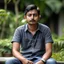 Placeholder: an 30 year old indian man, oval face, white skin, wearing shirt and jeans, sitting in a garden, peaceful, front face portrait, short hair, slightly muscular built, handsome