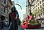 Placeholder: multi colored, bright, vivid, psychedelic, high detailed, high gloss, insanely detailed, matte, horrorcore, lining the street, unsettling contrast, monument to death, live action shot grim reaper parade, pulling a jesus parade float