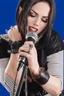 Placeholder: attractive female country music singer leaning forward while holding microphone in one hand, other hand brought up to side of neck, change clothing to plaid in natural tones, leather bracelets on wrists, long hair, mouth open singing, rings on fingers, eyes closed