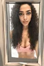 Placeholder: Generate a high-quality lifelike portrait of a 28-year-old Egyptian girl taking a cellphone selfie in the bathroom mirror. The POV should be from the perspective of the girl taking the selfie. She should have a slender body and be wearing skin-tight and very thig gym clothes. Her long black curly hair should be styled in a whimsical way. The photo should be captured using a 35mm film with a macro shot and shallow depth of field to create a bokeh effect. Professional lighting should be used, spec