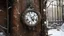 Placeholder: A melted clock hanging precariously on a rusty iron door, delicate thistles emerging from the cracks, scene set in a snowy winter landscape with a light dusting of snow on the clock and door.