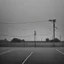 Placeholder: An empty carpark on a misty day. Telegraph poles and wires. Muted tones. Tilted horizon. With blotches, blurry areas and lens noise and grain. Hyper realistic Photo 4k