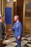 Placeholder: The Prince of Wales in traditional dress shakes hands with a guest in a blue suit, drawing room of St James's Palace, during a reception