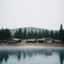 Placeholder: A polaroid photo of an odd room with structures. There is a group of fir trees in the background and a high hill in the distance. A lake. The surface below is in a pastel color. Fog is present.