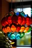 Placeholder: Hanging lampshade made out of mirrors that look like big petals of a flower, it has tinted glass, red, blue, orange,green