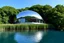 Placeholder: A sleek monolithic dome home with a glossy metallic facade and large glass windows, perched above a still water body. The structure integrates modern curved lines with the natural environment, surrounded by lush vegetation and offering a serene escape.