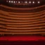 Placeholder: a single chair on stage under spotlight at a dark and empty symphony hall as seen from stage