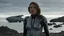 Placeholder: A woman in a catsuit standing on a beach of a rocky crystal-covered landscape with a crashed spaceship in the distance