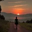 Placeholder: dark night, watching a woman from behind wearing a sleeveless dress who is walking towards a beautiful orange sunrise in the distance, mountains and forests around, photo quality