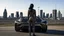 Placeholder: tall thin woman, with black straight hair, dressed in a camouflaged jumpsuit, looking out from the rear of a futuristic aircar, on a tarmac runway, with a city skyline in the distance