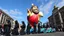 Placeholder: 200 ft tall floating cartoonish jesus parade balloon pulled by multiple grim reapers, multi colored, bright, vivid, psychedelic, high detailed, high gloss, insanely detailed, matte, horrorcore, lining the street, unsettling contrast, monument to death, live action shot grim reaper parade, pulling a jesus parade float