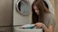 Placeholder: very confused young woman puts a few metal spoons inside the household dryer