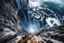 Placeholder: at the base of the rocky mountain peninsula, a great whirlpool waterfalls into deeper unknown depths