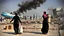 Placeholder: A Palestinian woman wearing a dress carrying very large bags of flour on her back, bending her back down in the destroyed Gaza City, and aid boxes descending from planes near the sea, with a large number of children looking up.