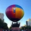 Placeholder: 200 ft tall floating cartoonish Jesus rendition hot air balloon pulled by multiple grim reapers, multi colored, bright, vivid, psychedelic, high detailed, high gloss, insanely detailed, matte, horrorcore, lining the street, unsettling contrast, monument to death, live action shot grim reaper parade, pulling a jesus parade float