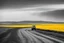 Placeholder: The yellow sky looms over the endless expanse of yellow fields in the West. The dusty road goes from left to right. A small red truck sits parked at two-thirds down the dusty road, a lone beacon of color against the monochrome landscape. The air is heavy with the scent of dry earth and distant memories, the sun beating down relentlessly, casting long shadows that stretch across the arid plains.