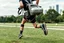 Placeholder: running jogger with an ersatz backpack pneumatic engine gadget with rubber hoses running into a futuristic cpap mask, vintage steel rod and metal hinge full leg calipers, absurd psychology, CO2 tanks, metaphoric situational photography, vestigial backpack exhaust pipe which is leaking fumes, background is a park with jogging trails, city skyline in distance