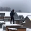 Placeholder: in the North of Canada, among neighbors in a small group of houses, an Afro-American man stands on the edge of the roof just before a snowstorm hits. He attaches plank plates to the roof to reinforce it, bracing for the impending storm. The cold air bites at his skin, the wind howling ominously, as he works diligently to secure the roof against the fury of the upcoming blizzard. The eerie silence of the snow-covered landscape amplifies the sound of his hammer, echoing through the quiet neighbo