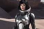 Placeholder: Photo of a Sci-fi woman, with black hair, wearing a silver and black spacesuit looking like an android, on an alien planet