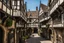 Placeholder: Old English Tudor Alley with shops, signs, bridges, and balconies, sunny day, warped and grubby