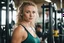 Placeholder: A candid, documentary-style photograph captured on high-grain 35mm film, shot from a low angle within a busy, sweat-drenched, working-class gym. The photo focuses on Kayden Kross, personifying youthful athletic Celtic energy. She is positioned naturally, casually navigating through complex weight machines, her gaze looking confidently off-camera as she moves with inherent grace. Her complex, multiple braids cascade down her back, catching the light and highlighting her movement. She is wearing l
